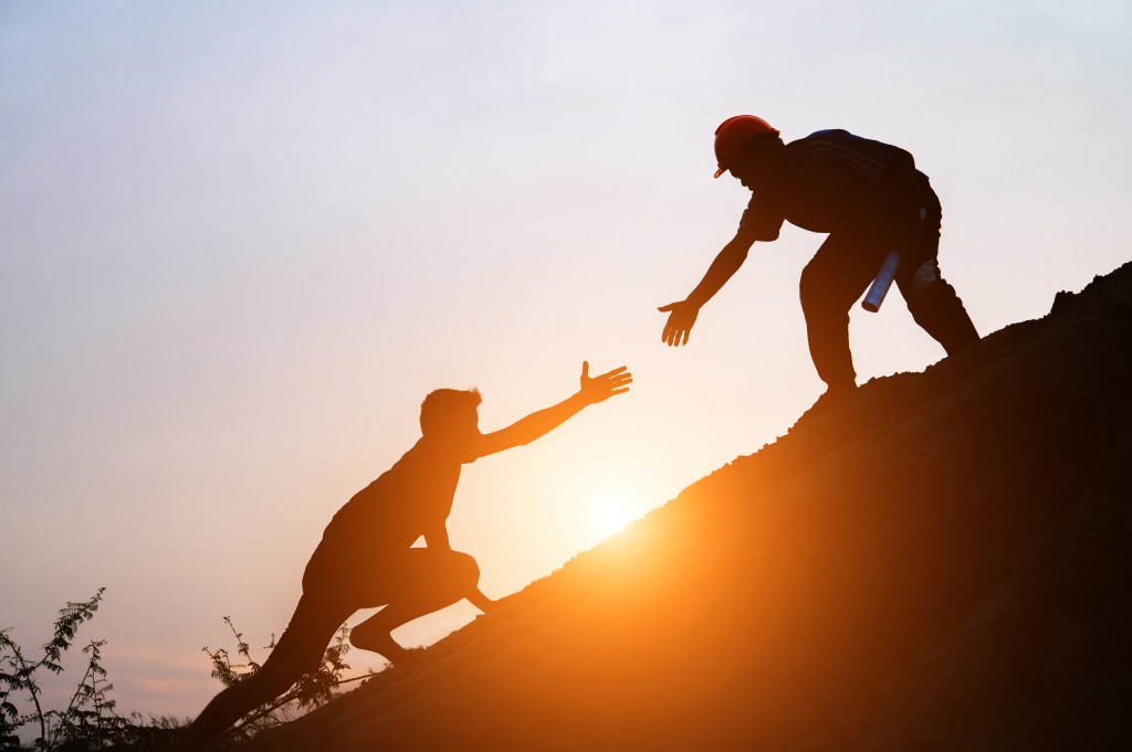 Tourists go up the hill in the sunrise to shake hands The male traveler shakes the hand of the male traveler who is climbing to the top of the hill 
